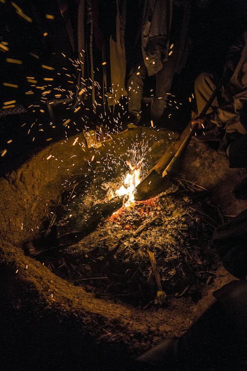 From above crop faceless male extinguishing bonfire with bright sparks with shovel in forest at night