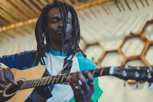 Free A talented black male musician plays an acoustic guitar indoors, showcasing his dreadlocks and artistic style. Stock Photo