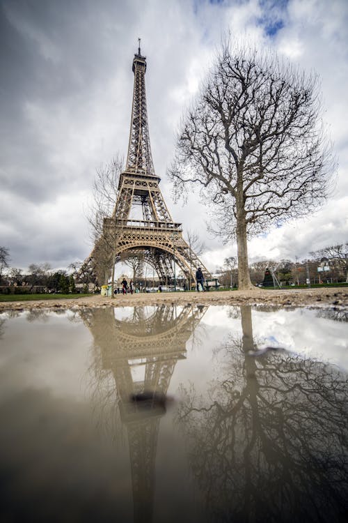 Low angle famous majestic Eiffel Tower located in center of Paris reflecting in muddy water with cloudy sky