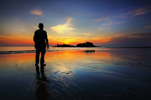 бесплатная Силуэт человека, стоящего на берегу моря Стоковое фото