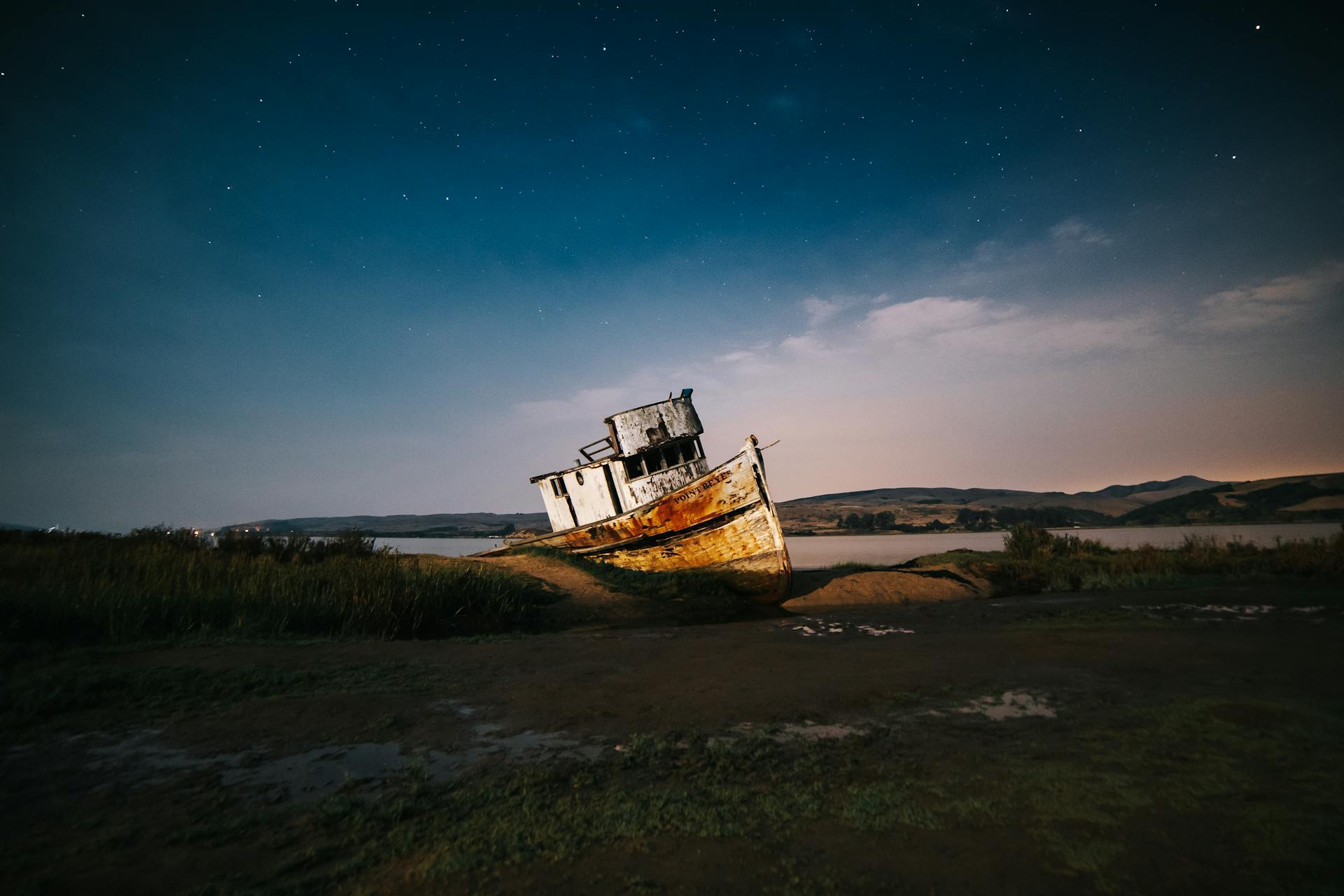 A dramatic view of a rusty shipwreck resting under a stunning starry night sky in a serene California landscape.