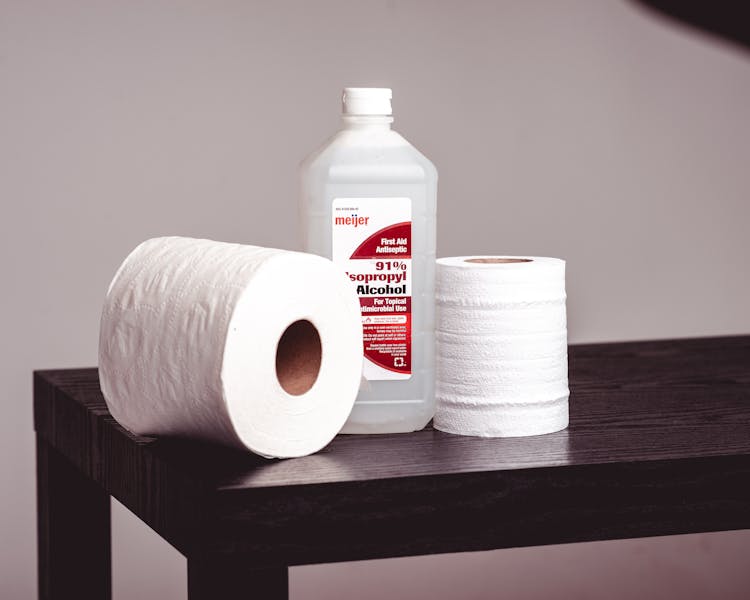 A Pair Of Tissue Rolls And A Bottle Of Isopropyl Alcohol On A Wooden Bench