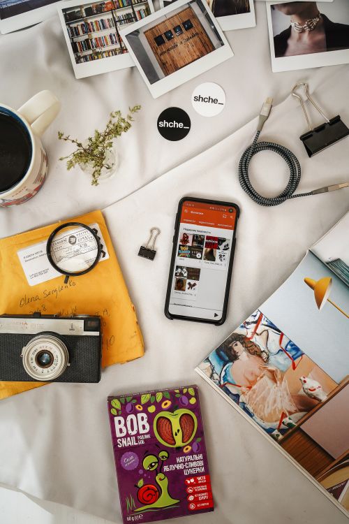 Free Flatlay showcasing vintage camera, mobile phone, magazines, and more on a cozy setting. Stock Photo