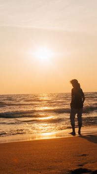 A lone person walks along the beach at sunset, with a tranquil ocean backdrop.