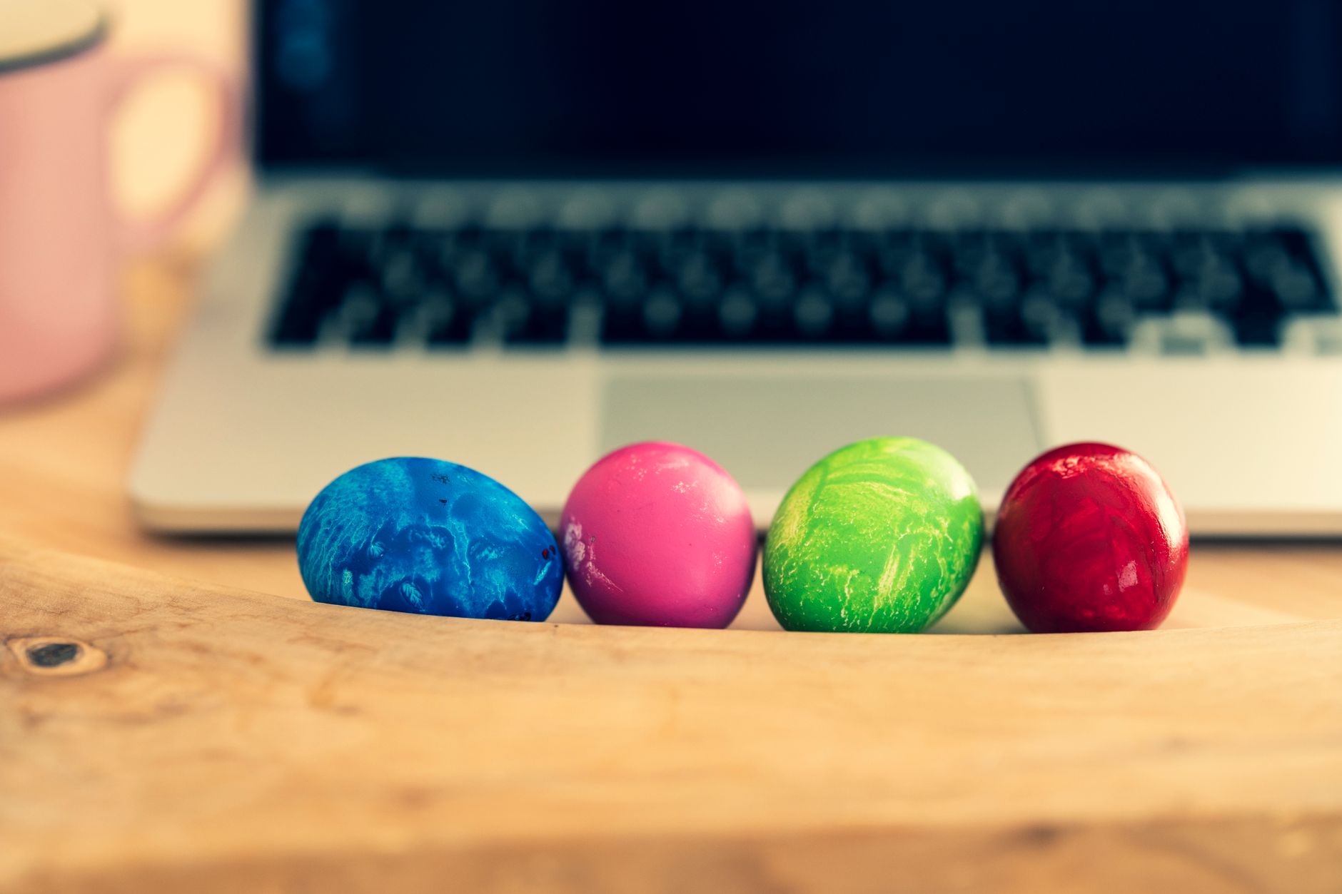 Vibrant Easter eggs on a wooden table beside a laptop. Perfect for spring decor ideas.