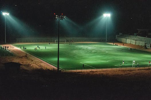 A vibrant nighttime soccer match in an illuminated stadium in Paro, Bhutan, captured from an elevated angle.