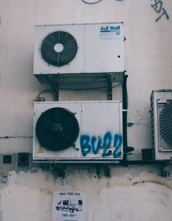 Low angle of weathered dirty air conditioner boxes installed on shabby wall of building on street