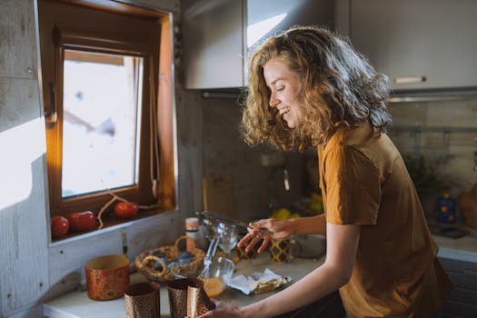 A happy woman with curly hair preparing food in a sunlit kitchen.
