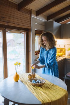 一名妇女在室内装饰复活节蛋糕，桌子旁摆着蓝鸡蛋