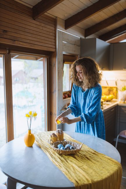 Woman decorating Easter cake indoors beside a table with blue eggs.