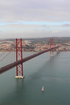 Aerial view of Lisbon's iconic 25 de Abril Bridge crossing the Tagus River on a cloudy day.