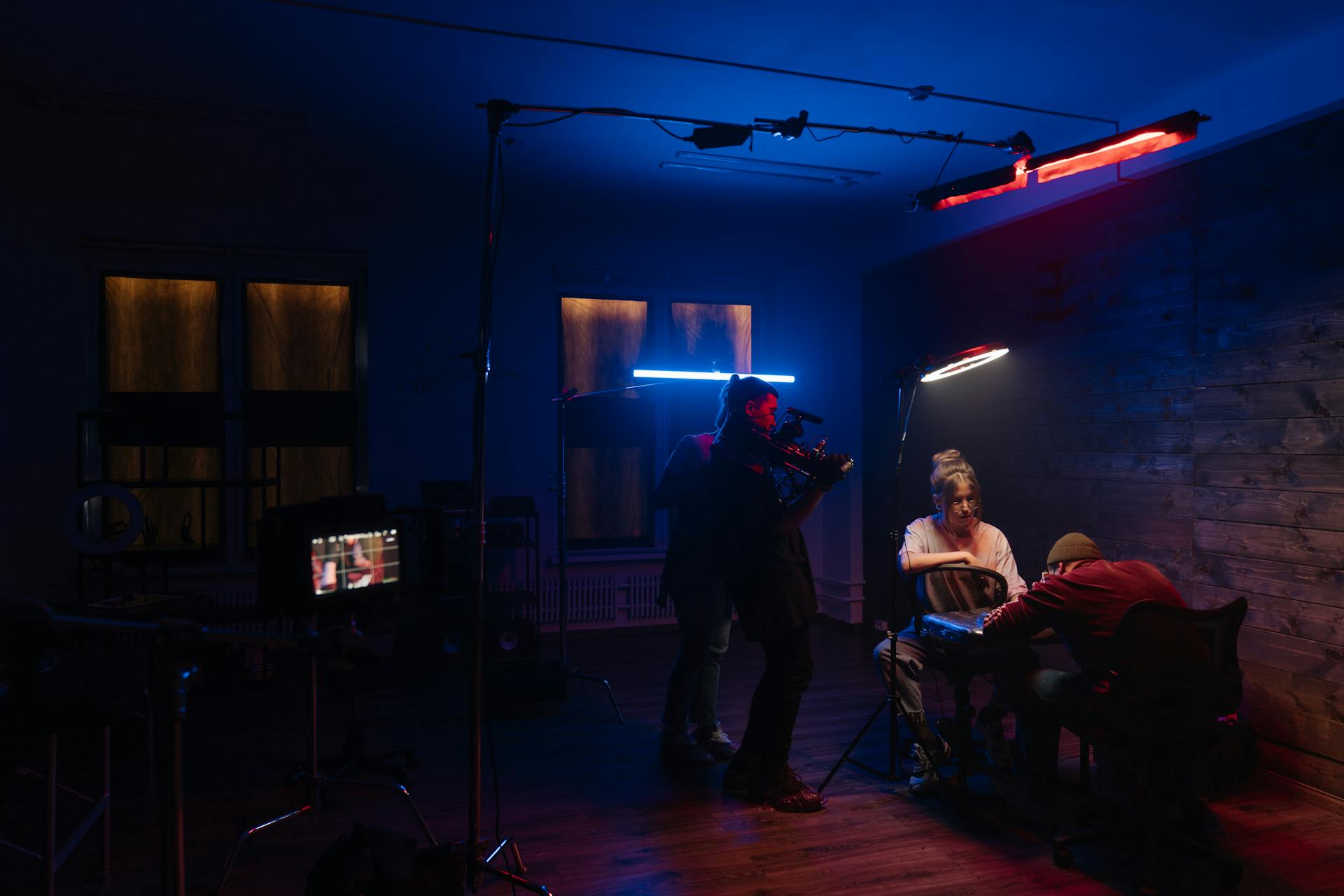 A tattoo artist tattooing a client in a dimly lit studio with neon lights and a camera crew filming the process.