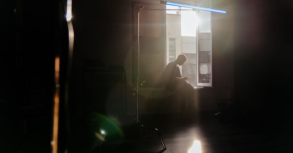 Silhouette of a man sitting by a window in a dimly lit creative studio.