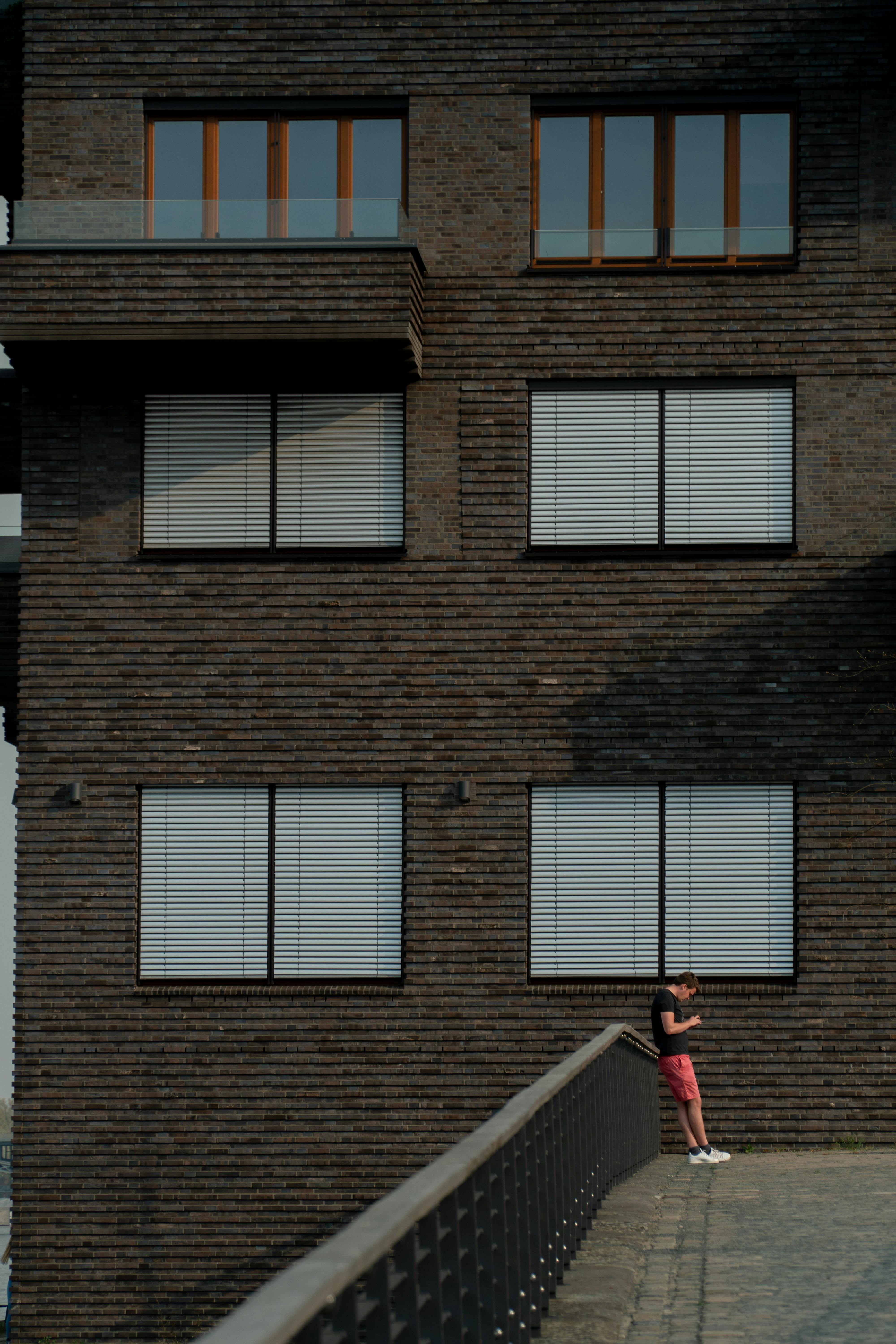 anonymous young man resting on footbridge against brick building