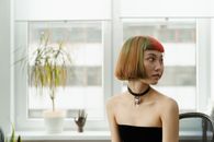 一位优雅的亚洲女性，发色缤纷，生活在自然光线充足的现代纹身工作室里