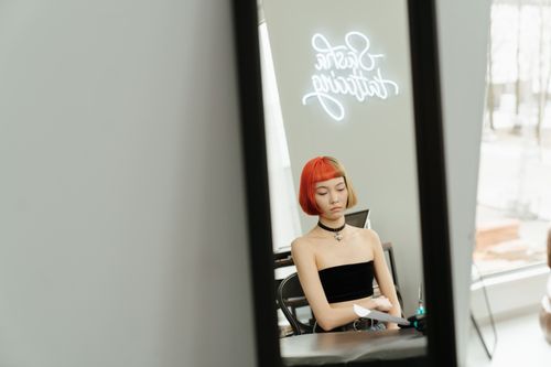 Free Portrait of a woman with colored hair sitting in a studio with neon lights visible in mirror reflection. Stock Photo