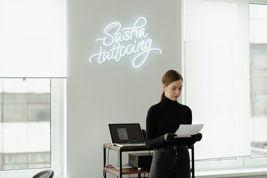A tattoo artist standing in a stylish studio with neon signage.