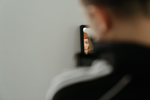 A woman with red hair is seen through her reflection in a mirror, indoors.