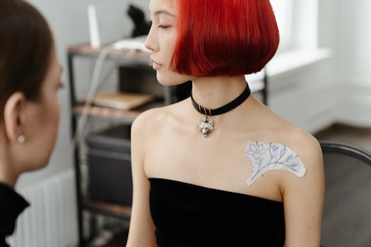 Asian female artist with red hair transfers floral tattoo design. Indoors styling.
