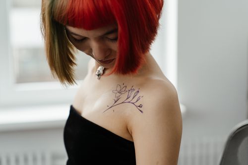 Free Asian woman with colorful hair showcasing floral tattoo design on shoulder in tattoo studio. Stock Photo