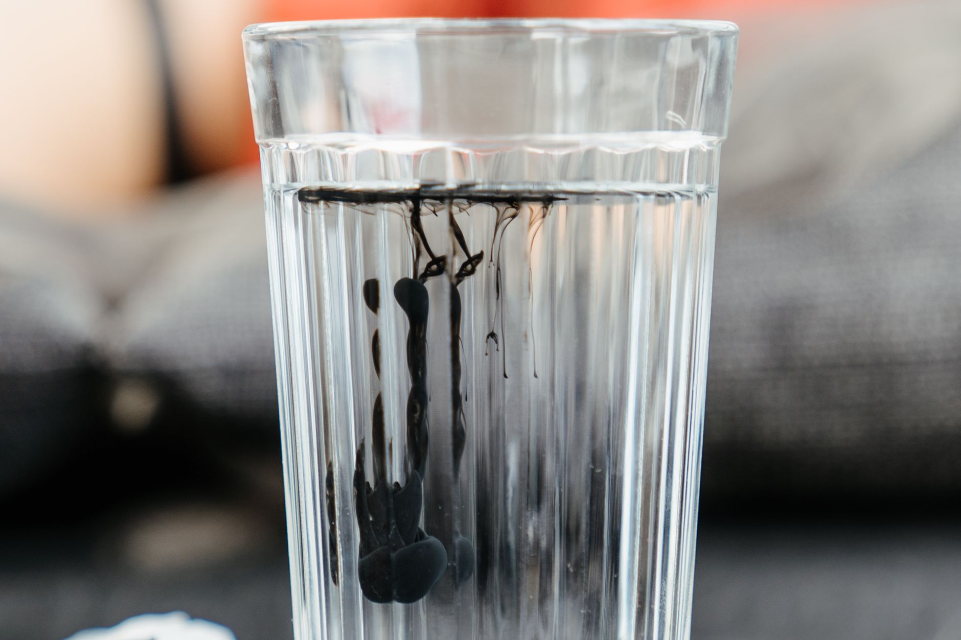 Close-up of black ink dissolving in a glass of clear water, creating artistic patterns.