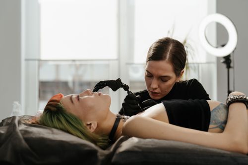 Free A skilled tattoo artist intricately inking a design on a client's arm in a well-lit, modern studio. Stock Photo