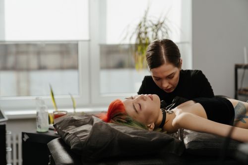 Free Tattoo artist working on client with vibrant hair in a sunlit studio. Stock Photo