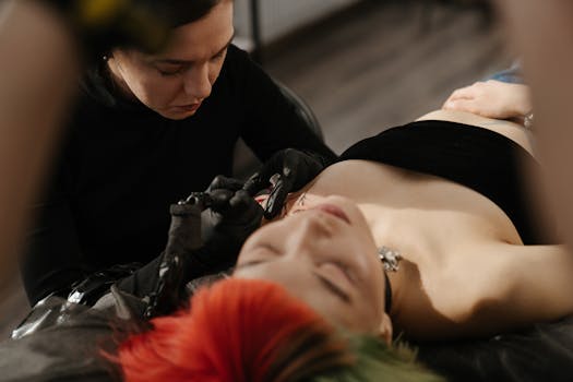 A tattoo artist works on a client in a tattoo studio, focusing on intricate design.