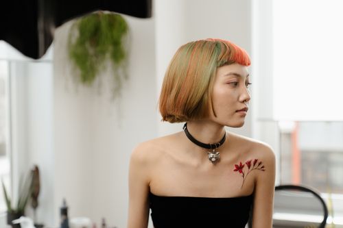 Free Profile portrait of a stylish woman with colorful hair and shoulder tattoo in a bright room. Stock Photo