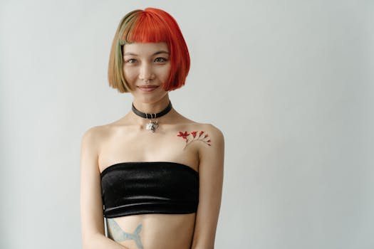 Portrait of an Asian woman with a shoulder tattoo and vibrant hair colors, showcasing modern style.