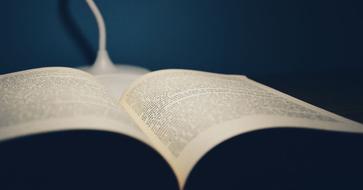 An open book on a table under the soft glow of a desk lamp, creating a study atmosphere.