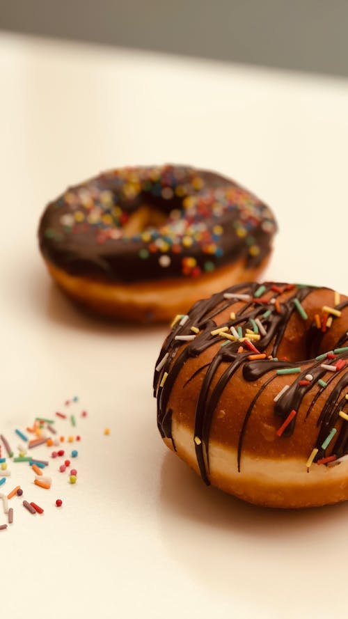 Tasty doughnuts with chocolate topping and colorful sprinkles arranged on white table in kitchen
