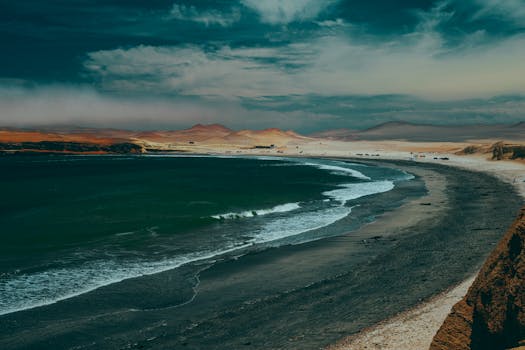 Stunning coastline with desert dunes under a dramatic sky, creating a tranquil natural scene.