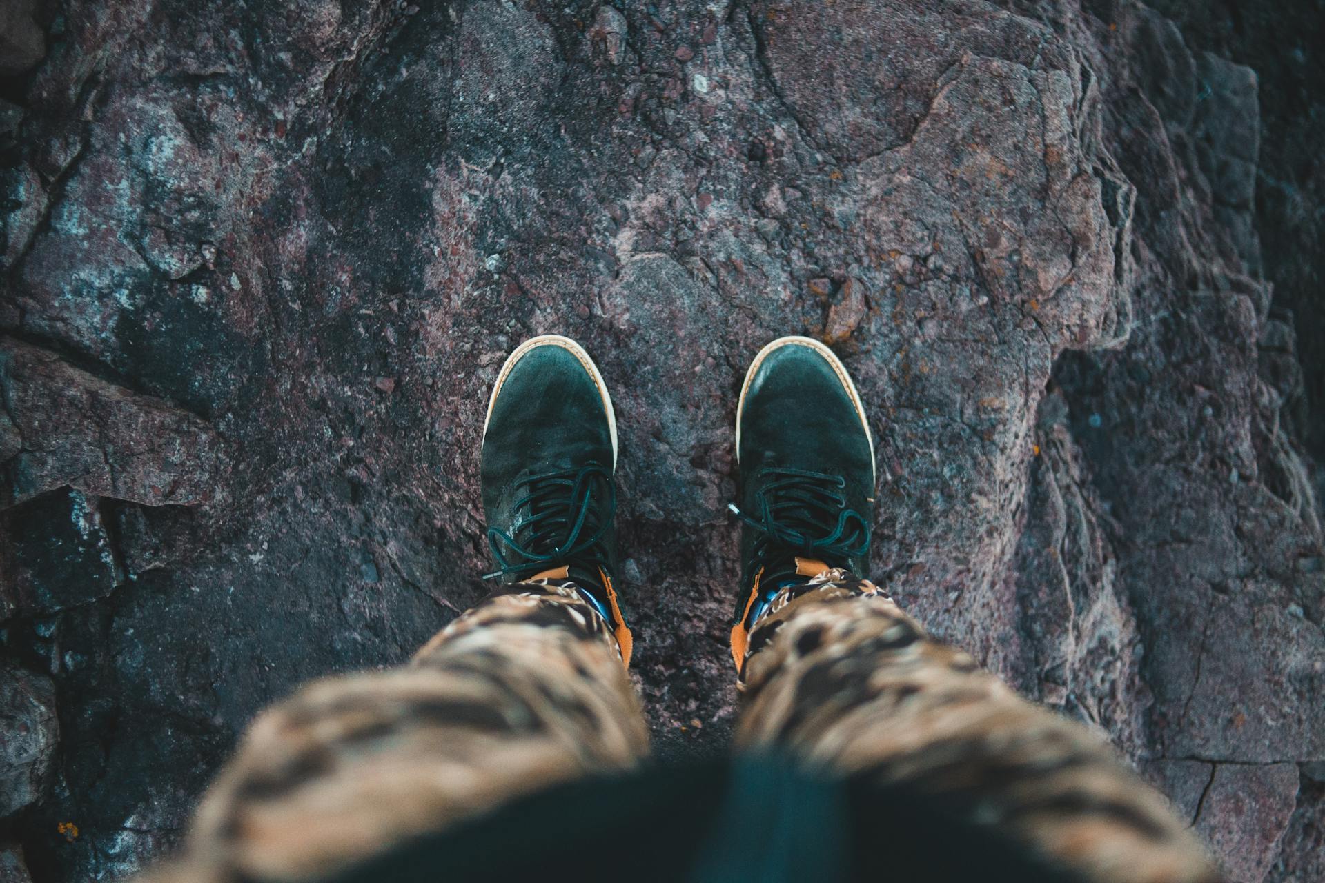 From above of crop anonymous anonymous traveler in stylish sneakers standing on top of rough rocky cliff and admiring view