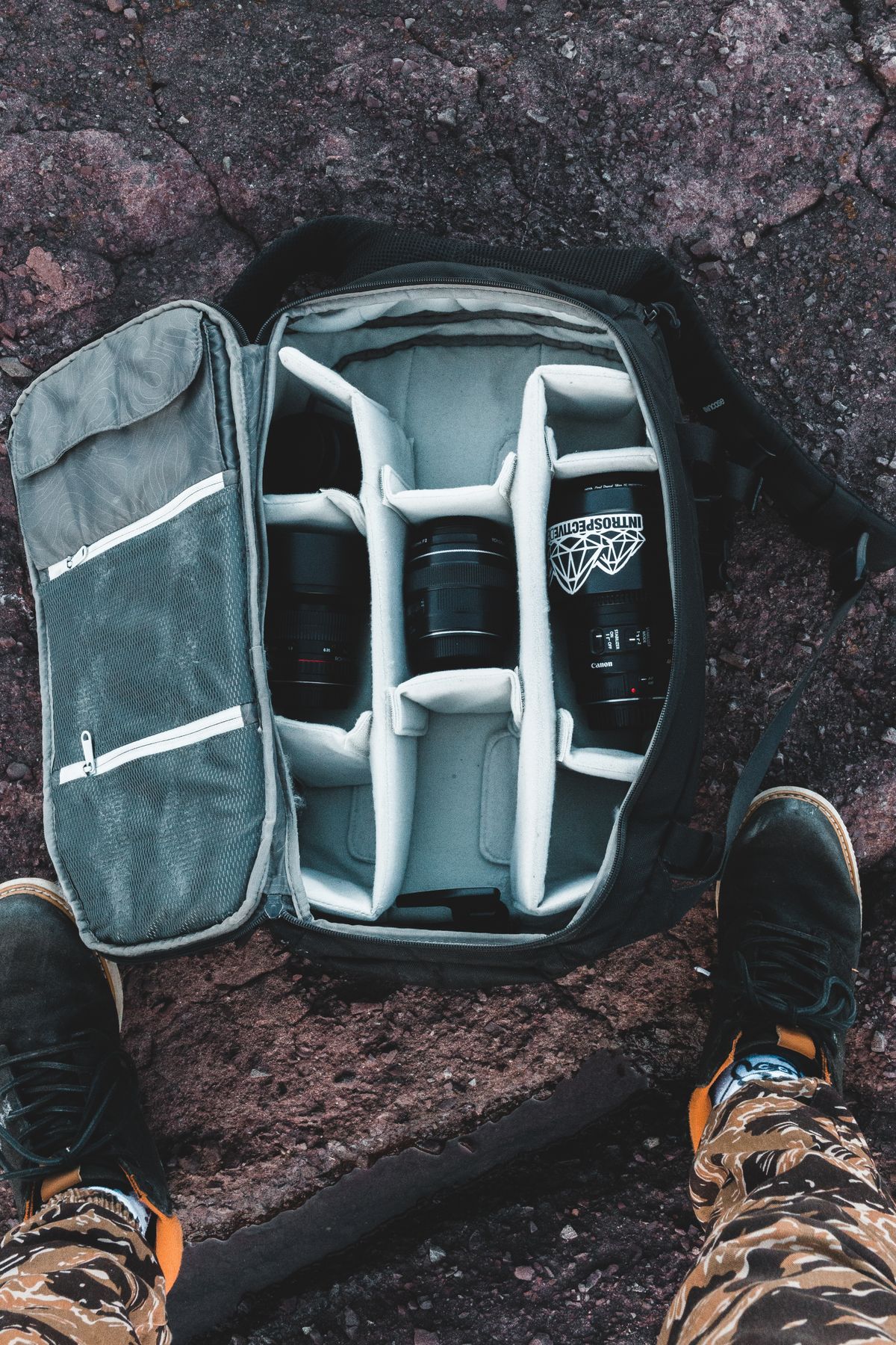 Camera gear bag left open on rocky outdoor ground, illustrating exposure to dust, sand, and environmental elements