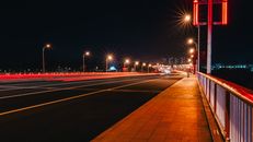 夜晚，明亮的桥梁上，过往车辆划出的灯光轨迹，展现了城市的活力与速度