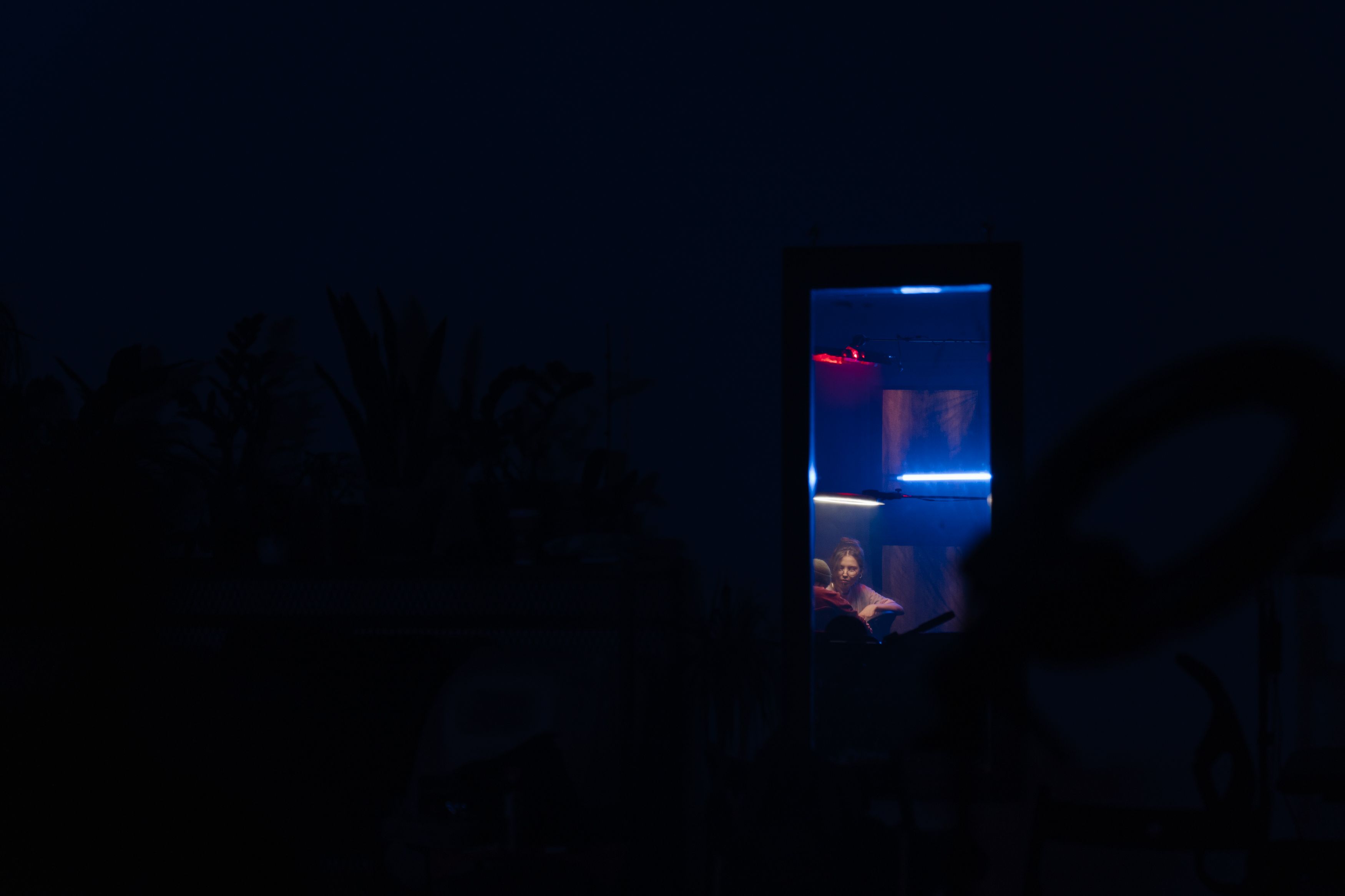 夜晚，一个女人坐在发光的盒子里，背景一片漆黑，营造出神秘的氛围