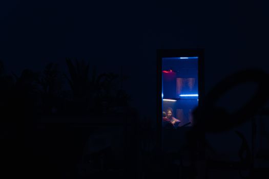 夜晚，一个女人坐在发光的盒子里，背景一片漆黑，营造出神秘的氛围