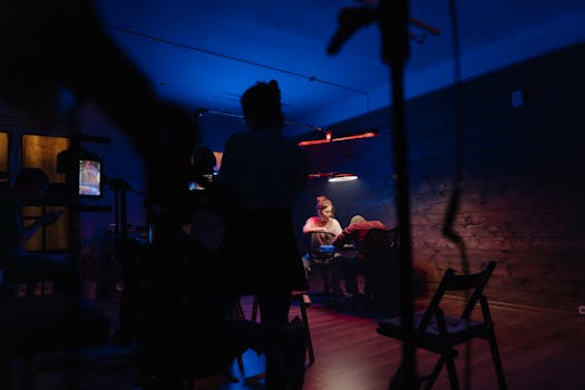 A creative team working in a neon-lit studio with camera equipment and electric lighting.