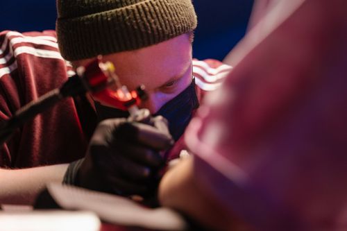 Free Tattoo artist in gloves concentrating on detailed tattoo work in a studio. Stock Photo