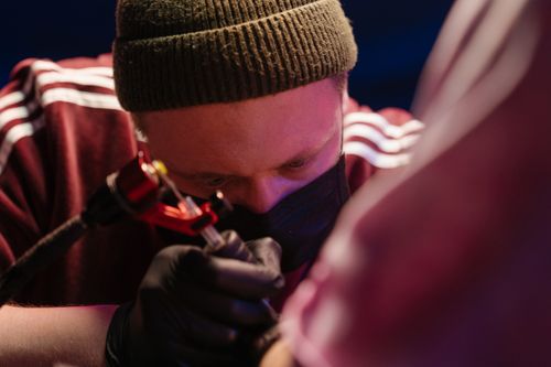 Free Tattoo artist concentrating while crafting intricate designs in a studio environment. Stock Photo