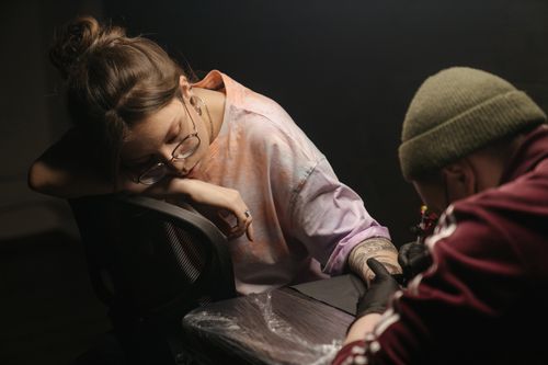 Free A woman patiently receiving a tattoo in a cozy, artistic tattoo studio. Stock Photo