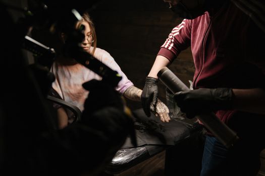 Tattoo artist applying ink to client's arm in a studio. Creative tattooing process.