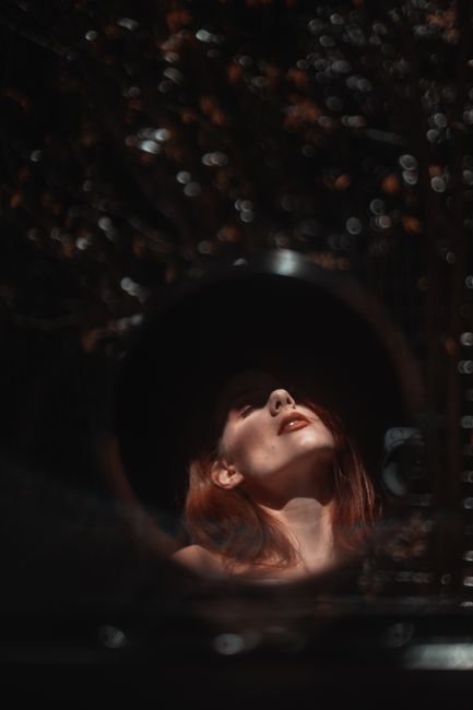 Reflection of young beautiful female with eyes closed in round mirror in dark room