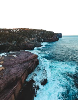 Breathtaking aerial view of rugged cliffs meeting the ocean in Flatrock, Canada.