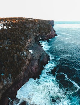 A stunning aerial view of the rugged coastline in Flatrock, NL, Canada with crashing waves.