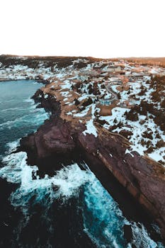 Stunning aerial shot of Flatrock, NL, Canada showing rugged cliffs and ocean waves during winter.