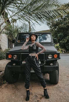 Fashionable woman in bucket hat poses confidently with SUV on a leisurely outdoor day.