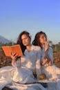 日落时分，两名身穿白色连衣裙的女子在户外读书，体现了宁静与优雅