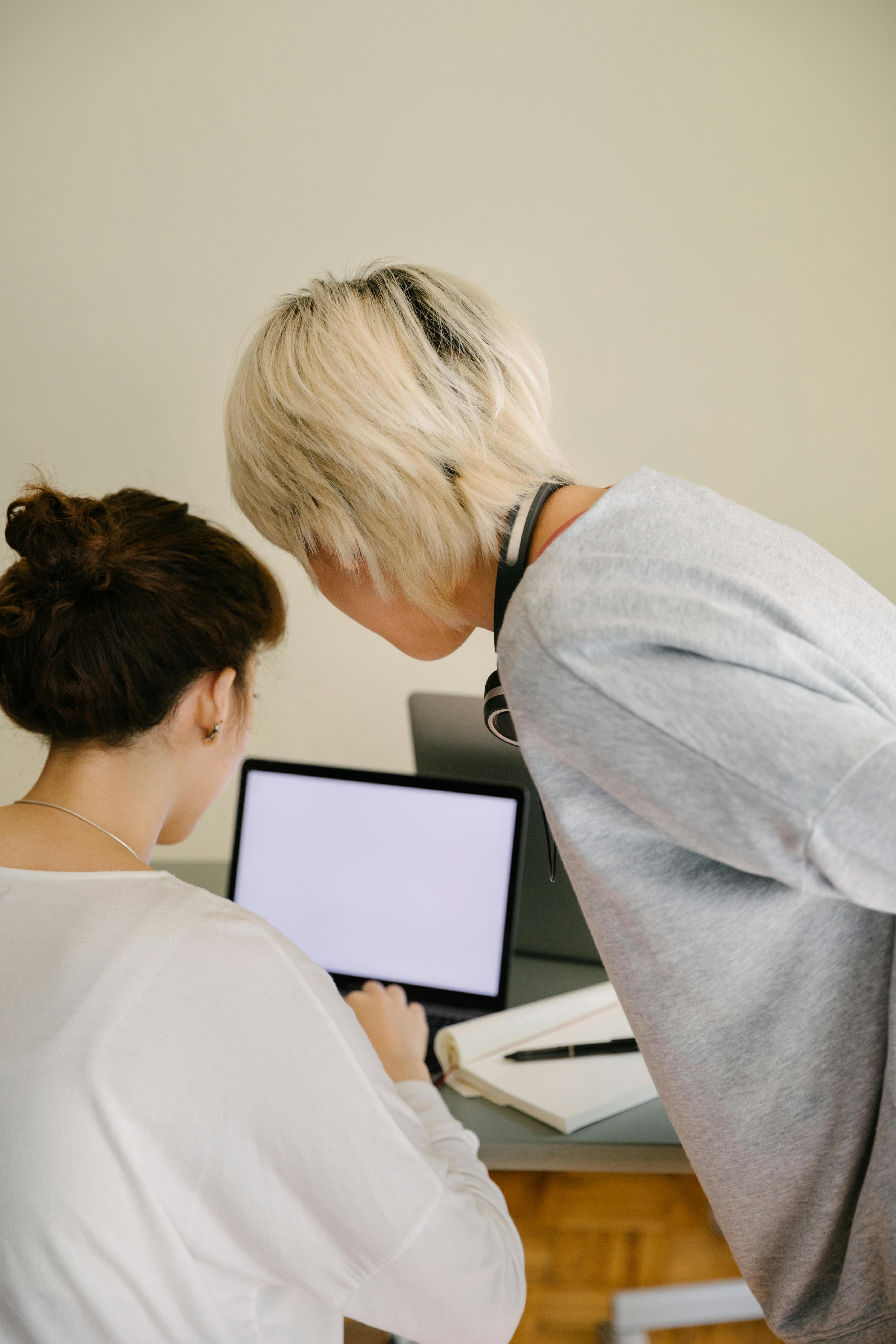 two women with a laptop, notepad, and pen.